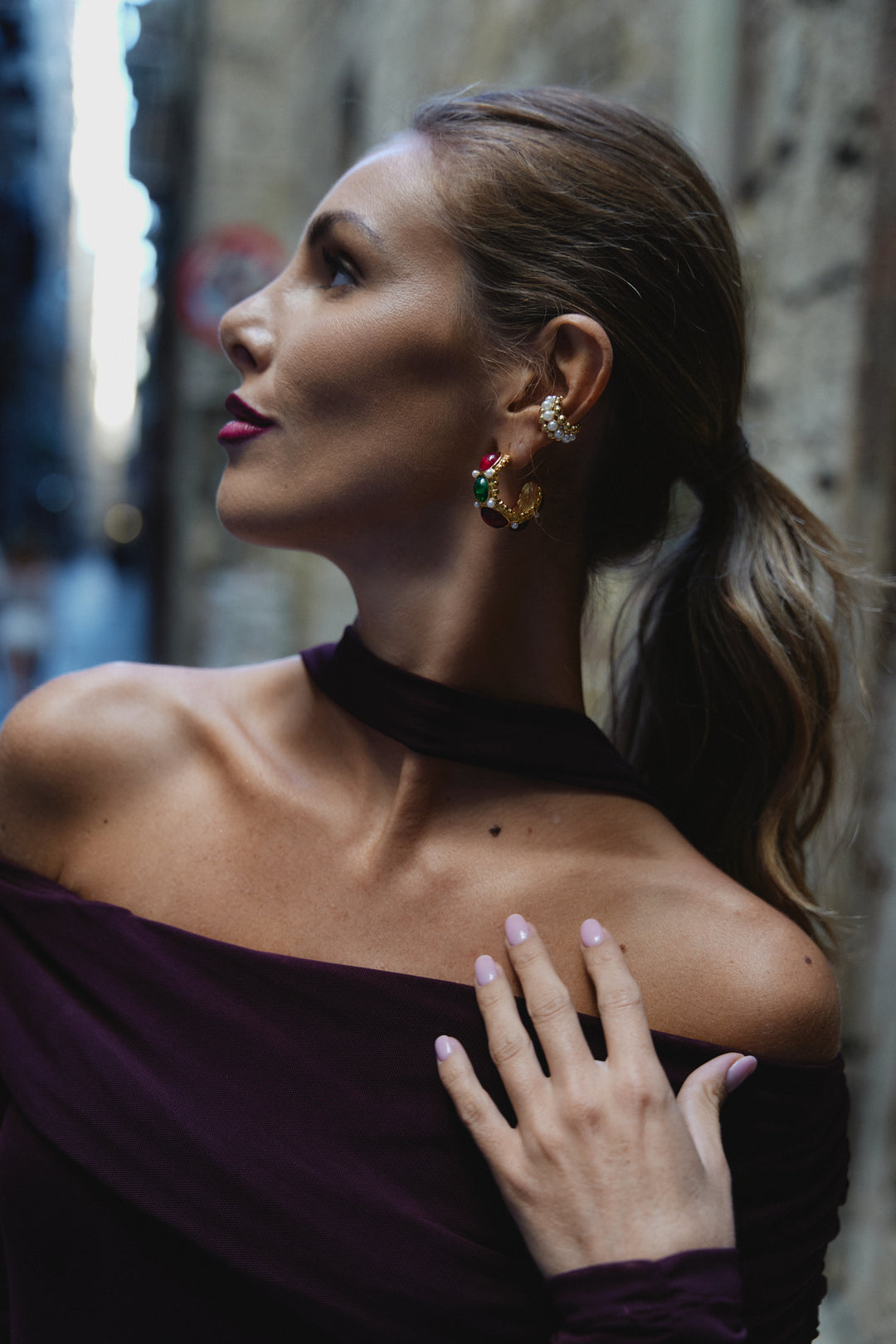 Earcuff Armonia, orecchino a cerchietto dorato con dettagli colorati, indossato sulla orecchio di una donna con capelli raccolti, sfondo urbano.